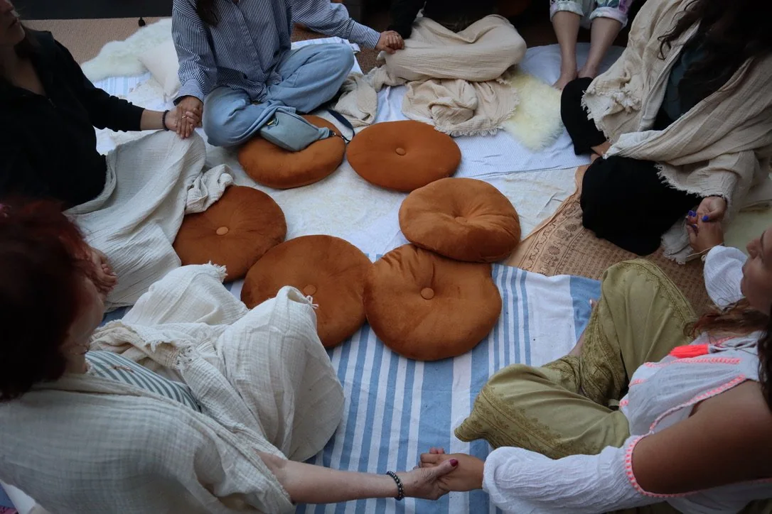 A circle of people seated on cushions on the floor