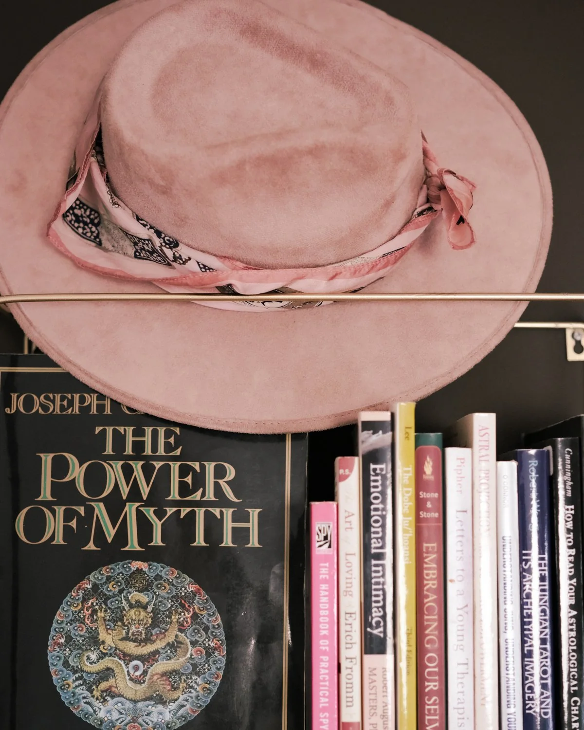 A pink hat resting on a shelf of books, including The Power of Myth